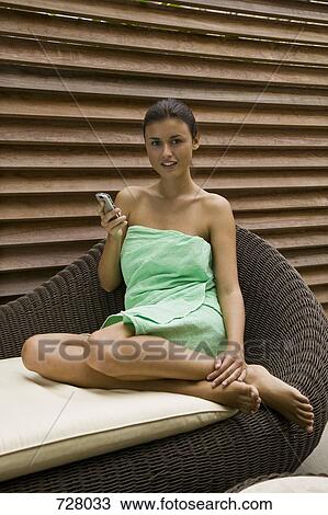 A woman sitting on a chaise lounge using a mobile phone View Large Photo Image Stock Image - A woman sitting on a chaise lounge using a mobile phone. Fotosearch
