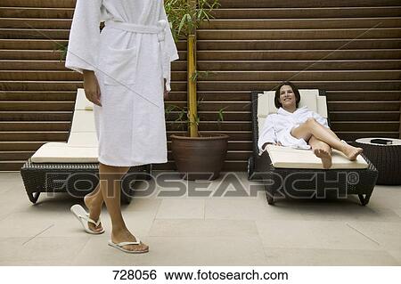 One woman lying in a lounge chair while another is walking away View Large Photo Image Stock Photograph - One woman lying in a lounge chair while another is walking away. Fotosearch