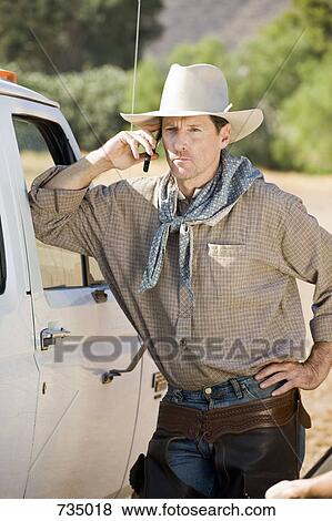 Stock Photo - A cowboy leaning against his car and talking in his mobile phone. Fotosearch
