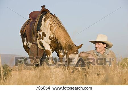 A cowboy sitting in long grass with his horse View Large Photo Image Picture - A cowboy sitting in long grass with his horse. Fotosearch