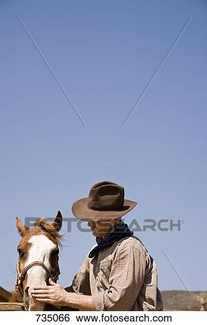 Stock Photograph - A cowboy stroking a horse. Fotosearch