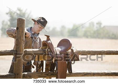 Stock Image - A rancher preparing a horse saddle on a fence. Fotosearch