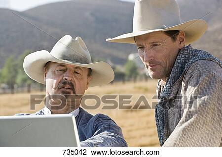 Two cowboys looking at a laptop together View Large Photo Image Stock Image - Two cowboys looking at a laptop together. Fotosearch