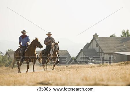 Stock Photography - Two cowboys riding horses through a field. Fotosearch