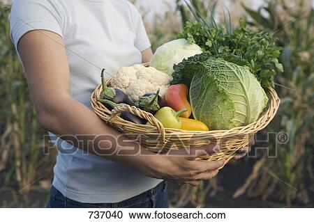 Stock Image - A teenage girl carrying a basket of vegetables. Fotosearch