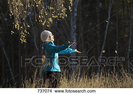 Picture - A young girl in a field catching leaves. Fotosearch