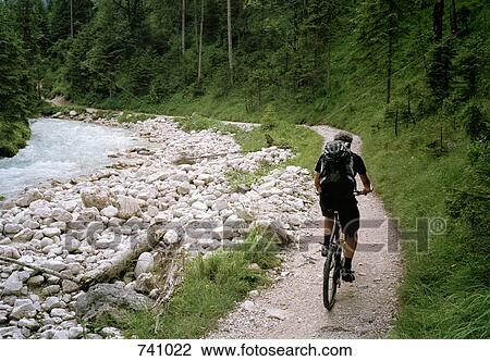 Stock Image - A man cycling alongside a river, Austria. Fotosearch
