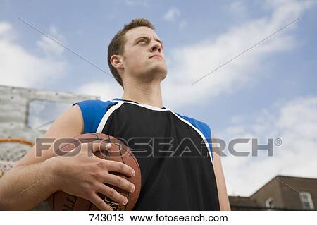 Stock Image - A basketball player holding a ball, portrait. Fotosearch