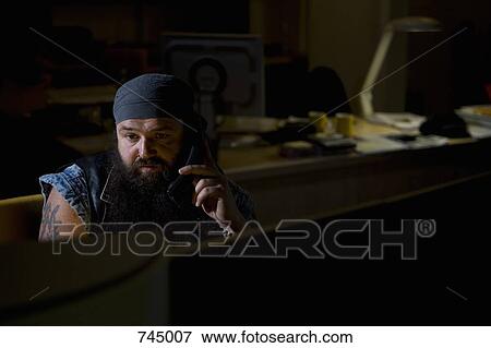 A biker sitting in a darkened office on the phone View Large Photo Image Stock Photo - A biker sitting in a darkened office on the phone. Fotosearch