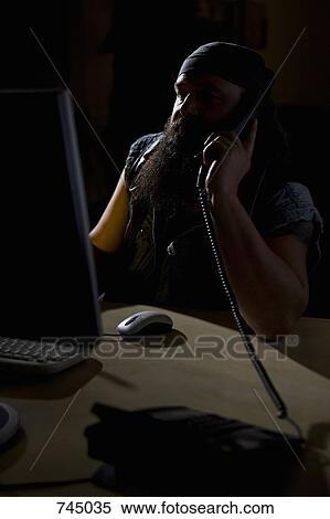 Stock Photography - A biker sitting in a darkened office on the phone. Fotosearch