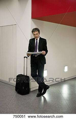 A businessman reading the newspaper and waiting with his suitcase View Large Photo Image Stock Image - A businessman reading the newspaper and waiting with his suitcase. Fotosearch