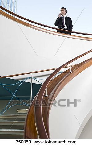 Stock Image - A businessman talking on his mobile phone at the top of a staircase. Fotosearch