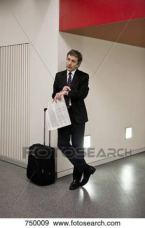 Stock Photo - A businessman waiting with his suitcase and holding a newspaper. Fotosearch
