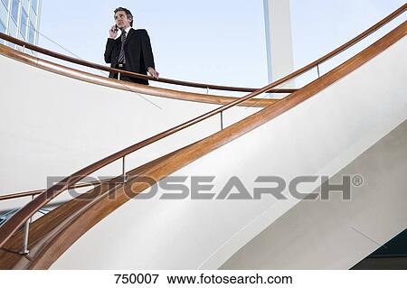Stock Photo - A man talking on his mobile phone at the top of a staircase. Fotosearch