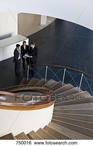 Three business people standing at the bottom of a staircase View Large Photo Image Stock Photograph - Three business people standing at the bottom of a staircase. Fotosearch