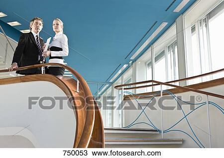 Stock Image - Two business people standing at the top of a staircase. Fotosearch
