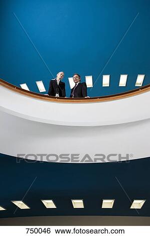 Two business people standing on a balcony View Large Photo Image Stock Photograph - Two business people standing on a balcony. Fotosearch