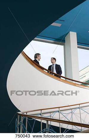 Stock Image - Two businessmen standing at the top of a staircase talking. Fotosearch