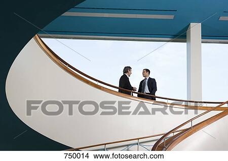 Two businessmen standing on a balcony and talking View Large Photo Image Picture - Two businessmen standing on a balcony and talking. Fotosearch