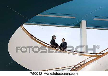 Two businessmen standing on a balcony and shaking hands View Large Photo Image Stock Image - Two businessmen standing on a balcony and shaking hands. Fotosearch
