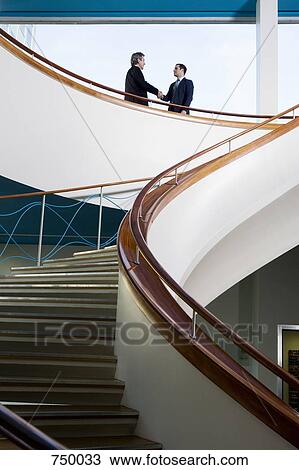 Two businessmen standing on a balcony and shaking hands View Large Photo Image Stock Image - Two businessmen standing on a balcony and shaking hands. Fotosearch