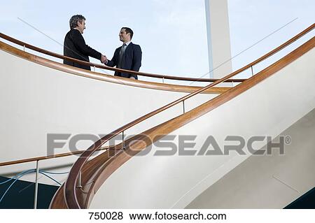 Two businessmen standing on a balcony and shaking hands View Large Photo Image Stock Photo - Two businessmen standing on a balcony and shaking hands. Fotosearch