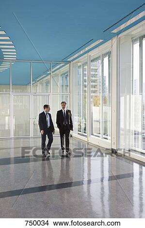 Two businessmen walking in the foyer of a convention center View Large Photo Image Picture - Two businessmen walking in the foyer of a convention center. Fotosearch