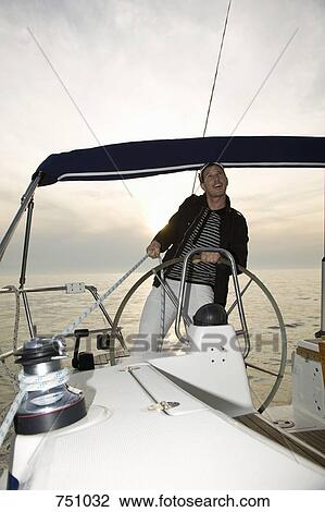 Stock Image - A man at the helm of a yacht adjusting the rigging. Fotosearch