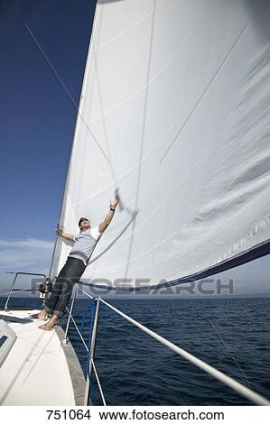 Picture - A man leaning against the sail of a yacht. Fotosearch