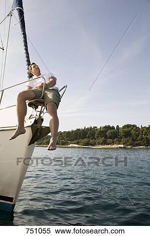 Stock Photography - A man sitting on the bow of a yacht. Fotosearch