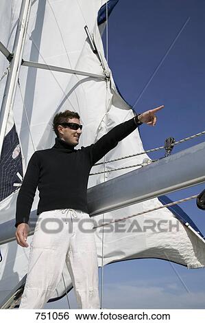 Stock Photograph - A man standing on a yacht and pointing. Fotosearch