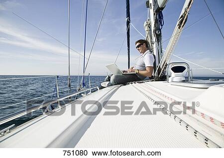 Stock Image - A man using a laptop on a yacht. Fotosearch