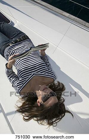 Stock Image - A woman lying down and reading on a yacht. Fotosearch
