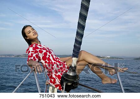 Stock Image - A woman sitting on the bow of a yacht. Fotosearch