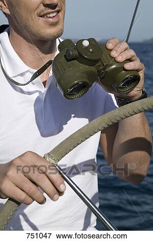 Detail of a man with binoculars at the helm of a yacht View Large Photo Image Stock Photo - Detail of a man with binoculars at the helm of a yacht. Fotosearch