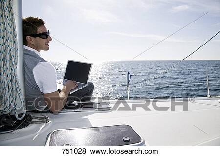 Rear view of a man using a laptop on a yacht View Large Photo Image Stock Photo - Rear view of a man using a laptop on a yacht. Fotosearch