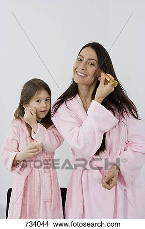 Picture - A mother and daughter in pink bathrobes applying make up. Fotosearch