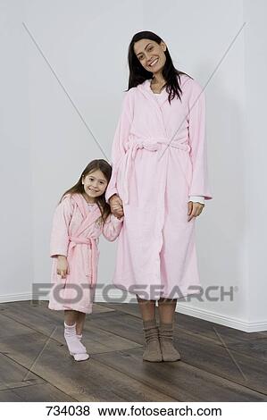 Stock Photo - A mother and daughter wearing pink bathrobes holding hands. Fotosearch