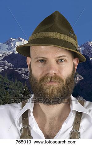 Stock Image - A man wearing an alpine hat and lederhosen with a mountain backdrop. Fotosearch