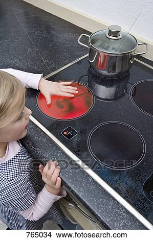 Picture - A young girl holding her hand over a hot electric stove burner. Fotosearch
