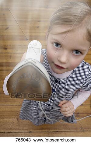 Stock Image - A young girl holding up a steaming hot iron. Fotosearch