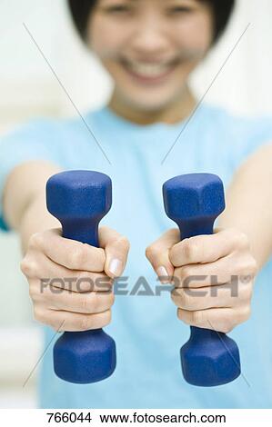Picture - A woman holding two dumbbells. Fotosearch