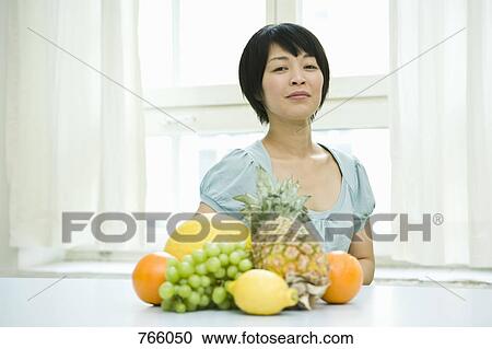 Stock Image - A woman sitting behind fruit on a counter. Fotosearch