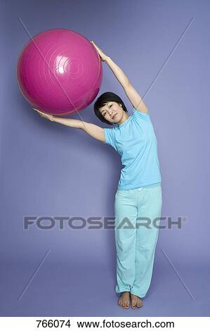 Picture - A woman standing and holding a fitness ball. Fotosearch