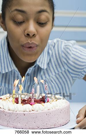 Stock Photo - A young woman blowing out candles on a birthday cake. Fotosearch