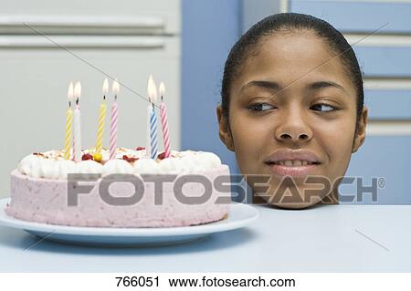 Stock Image - A young woman peeking at a birthday cake. Fotosearch