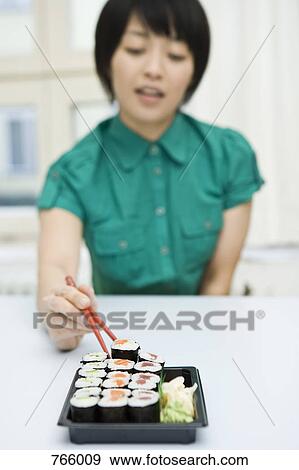 A young woman sitting at a table and eating sushi View Large Photo Image Stock Photo - A young woman sitting at a table and eating sushi. Fotosearch