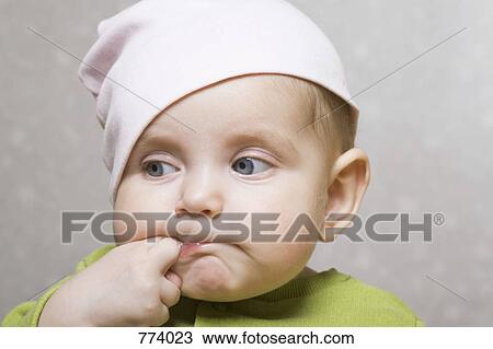 Stock Image - A baby girl sucking her fingers, portrait. Fotosearch