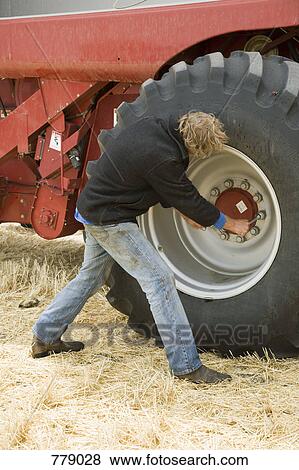 Stock Photo - A farmer fixing the wheel of a combine. Fotosearch