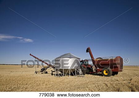 Stock Photo - A tractor and combine next to a seed container in a wheat field. Fotosearch